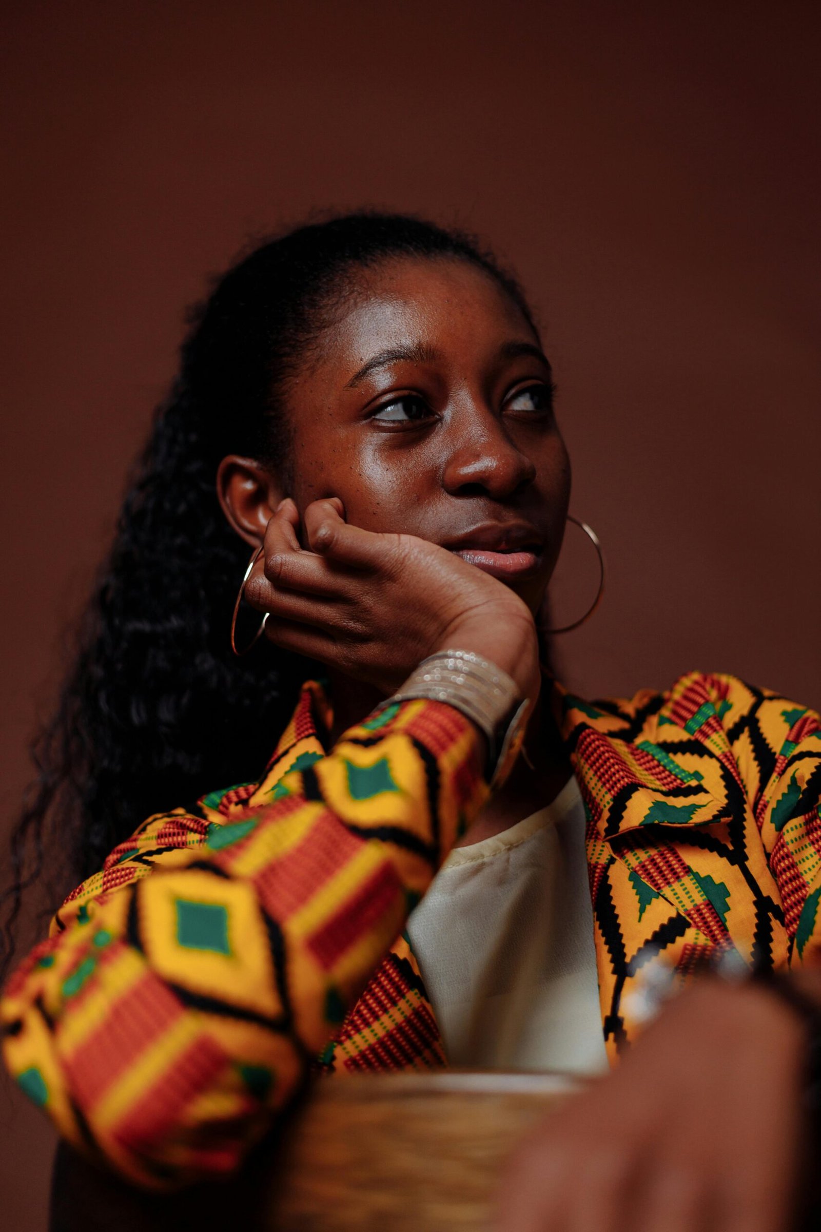 Portrait of a stylish woman posing against a brown background with tribal print blazer and hoop earrings.