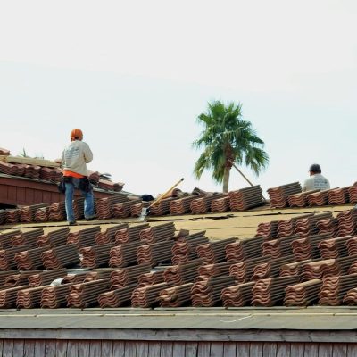 Construction workers installing terra cotta roof tiles under the sunny Phoenix sky.