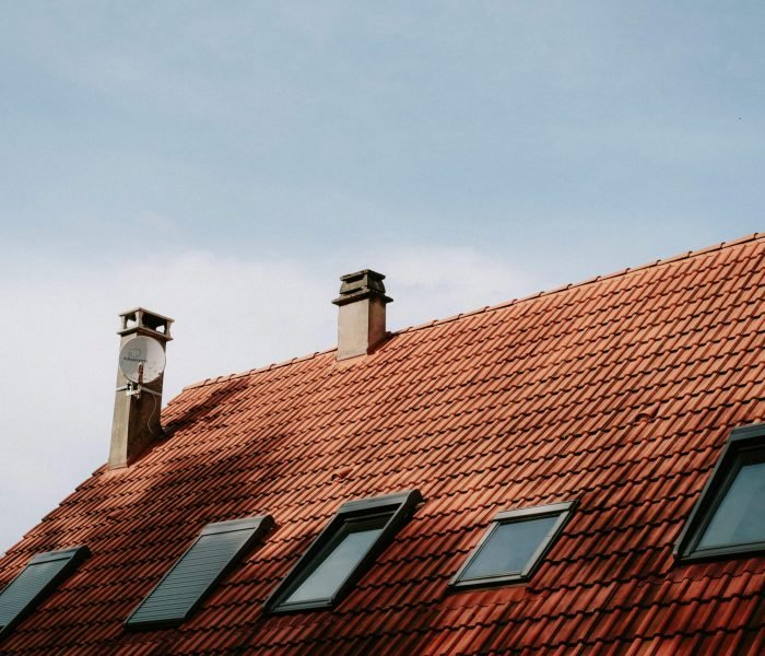 A picturesque red tiled roof featuring chimneys and skylight windows against a blue sky.