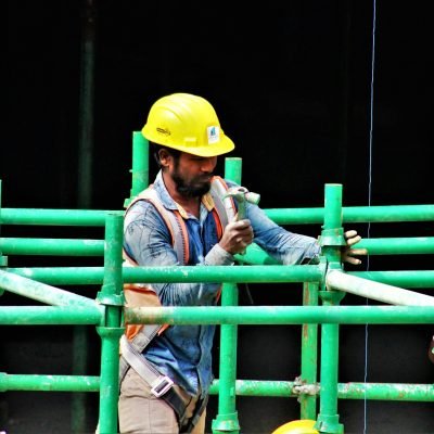A construction worker using a hammer to assemble green scaffolding on a building site.