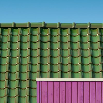 A close-up of a green tiled rooftop against a blue sky with a contrasting pink wall.