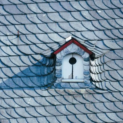 A detailed view of a slate rooftop with a central birdhouse surrounded by artistic tile patterns.
