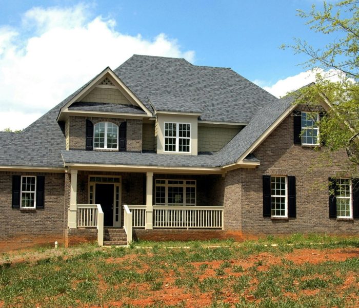Classic two-story brick house with gable roof and front lawn in suburban setting.