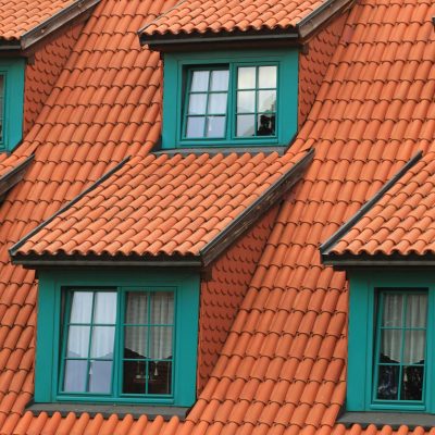 Close-up of an orange tiled roof with green framed dormer windows, creating a colorful architectural contrast.