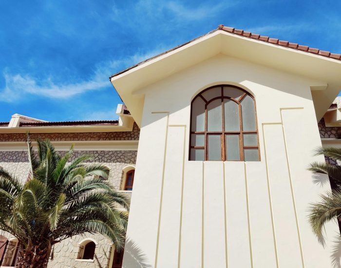 A stylish villa with large windows and palm trees under a bright blue sky.
