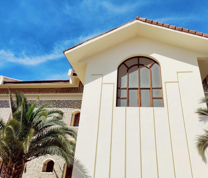 A stylish villa with large windows and palm trees under a bright blue sky.
