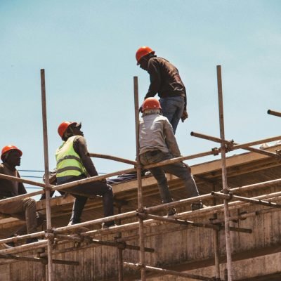 Construction workers wearing safety gear on scaffolding under clear skies in Nairobi, Kenya.