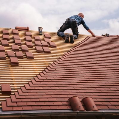 A roofer carefully installs shingles on a new residential roof under a cloudy sky.