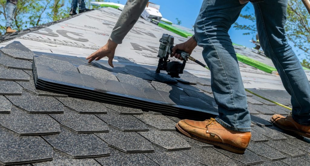 Roofer using nail gun for shingle installation on residential roof.