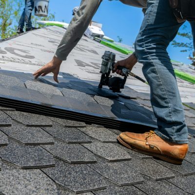 Roofer using nail gun for shingle installation on residential roof.