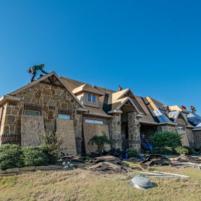 Brick house in Weatherford, Texas undergoing roof installation. Workers on roof under clear sky.