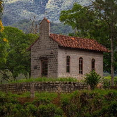 Charming stone chapel nestled in a tranquil forest with mountainous backdrop.