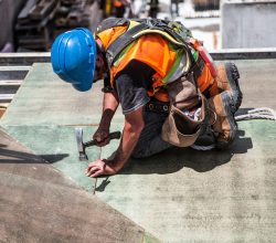 A skilled construction worker in protective gear hammering a rooftop panel.