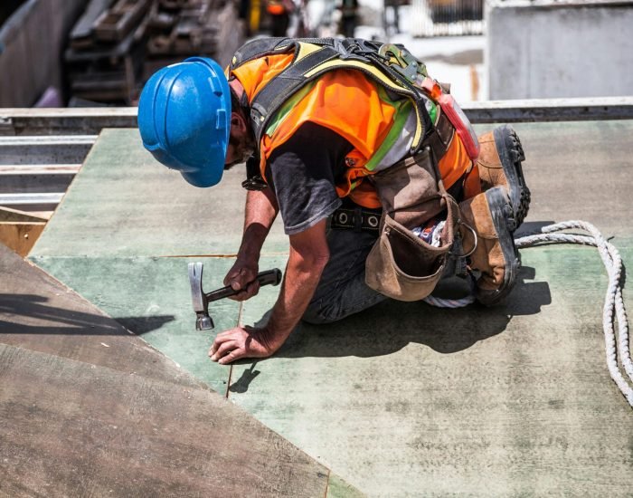 A skilled construction worker in protective gear hammering a rooftop panel.