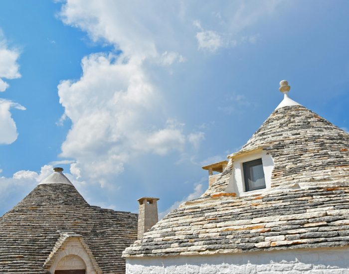Traditional trulli houses in Puglia with unique conical roofs under a vibrant blue sky.