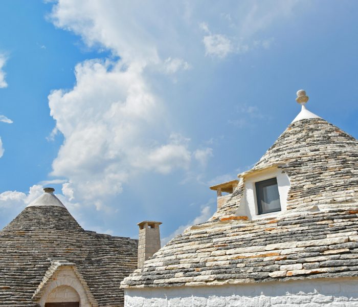 Traditional trulli houses in Puglia with unique conical roofs under a vibrant blue sky.