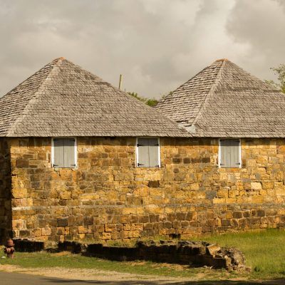 A rustic stone house with wooden shutters and a hipped roof set in a rural landscape.