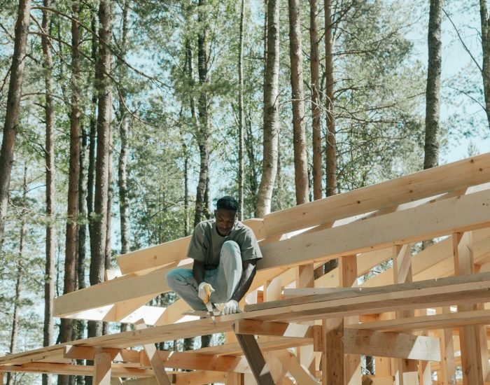 An adult man working on a wooden construction project in a sunny forest setting.