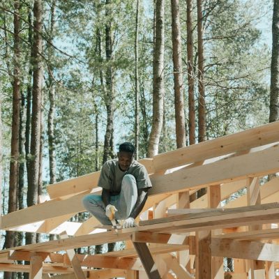 An adult man working on a wooden construction project in a sunny forest setting.