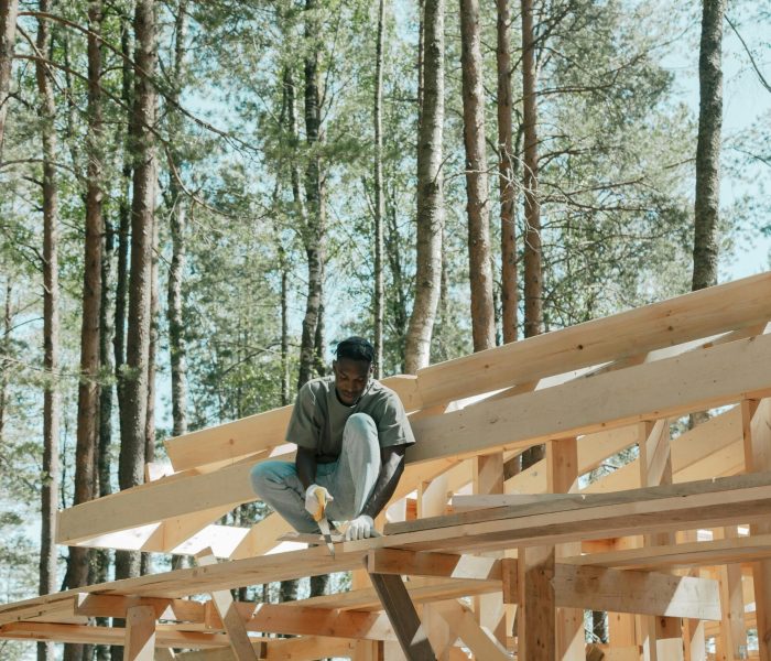 An adult man working on a wooden construction project in a sunny forest setting.