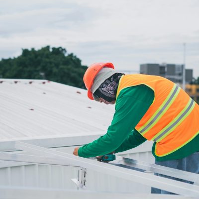 A construction worker wearing safety gear working on rooftop installation outdoors.