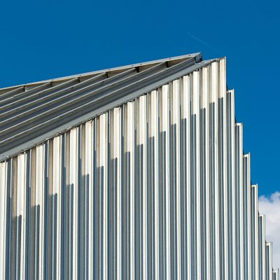Low angle shot of a modern building with a corrugated steel facade against a clear blue sky.